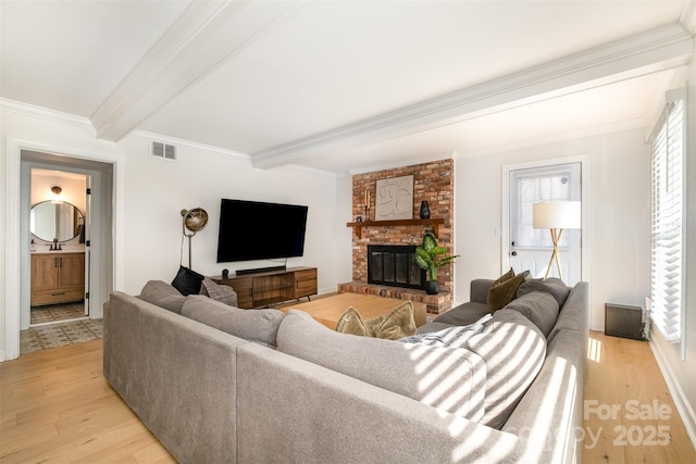 living room with visible vents, beamed ceiling, ornamental molding, light wood finished floors, and a brick fireplace