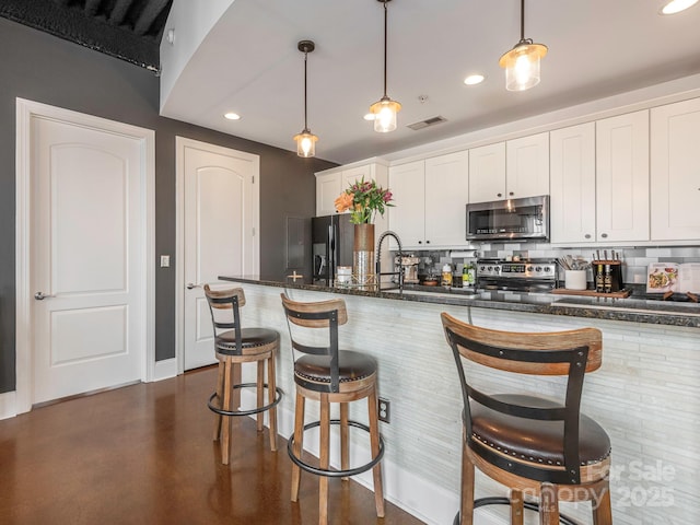 kitchen featuring visible vents, decorative backsplash, appliances with stainless steel finishes, white cabinetry, and a kitchen breakfast bar