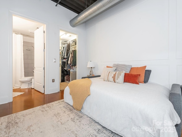 bedroom with connected bathroom, a closet, a spacious closet, and wood finished floors