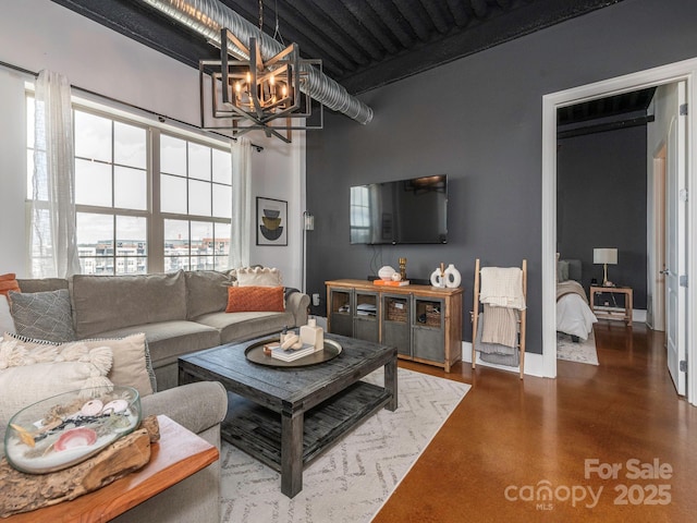 living area with a chandelier, beam ceiling, finished concrete flooring, and baseboards