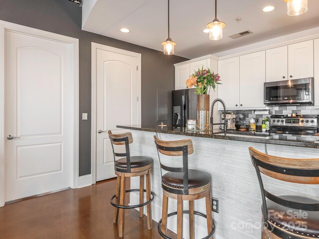 kitchen featuring visible vents, white cabinetry, appliances with stainless steel finishes, dark stone counters, and a kitchen bar