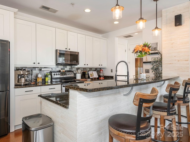 kitchen with white cabinets, stainless steel appliances, visible vents, and a kitchen breakfast bar