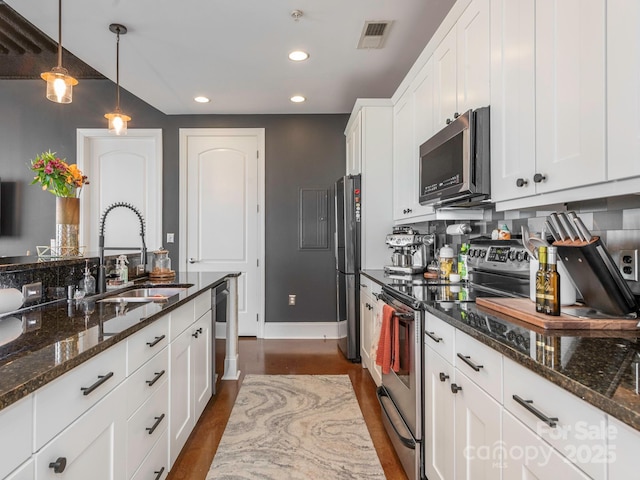 kitchen featuring visible vents, white cabinets, dark stone counters, stainless steel appliances, and a sink