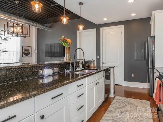 kitchen featuring white cabinets, dark stone counters, appliances with stainless steel finishes, decorative light fixtures, and a sink