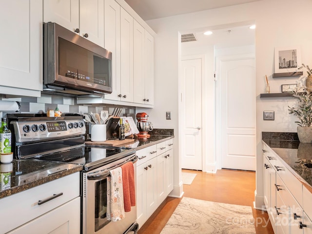 kitchen with stainless steel appliances, dark stone counters, white cabinetry, and backsplash