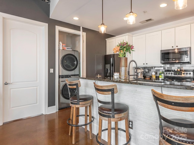 kitchen with visible vents, white cabinets, dark stone counters, stacked washer and clothes dryer, and stainless steel appliances