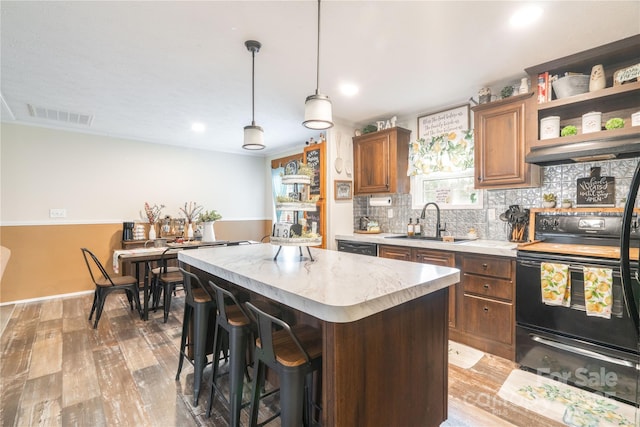 kitchen featuring electric range, visible vents, a center island, under cabinet range hood, and a sink