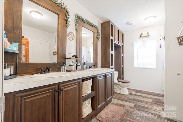 full bath with double vanity, ornamental molding, a sink, and wood finished floors