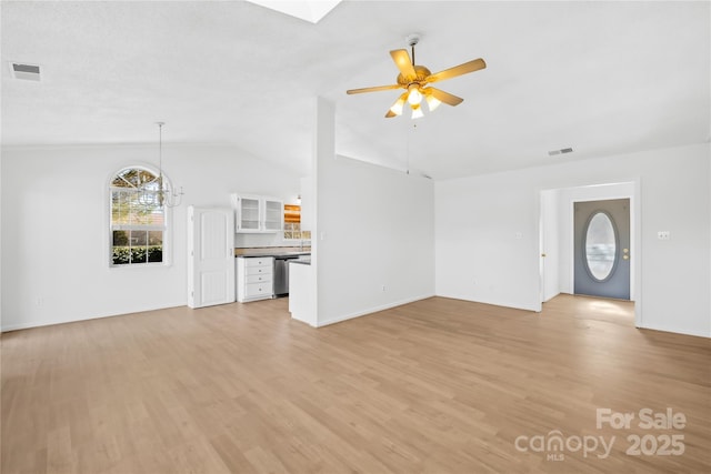 unfurnished living room featuring ceiling fan with notable chandelier, vaulted ceiling with skylight, light wood-type flooring, and visible vents