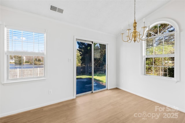 interior space with a notable chandelier, visible vents, vaulted ceiling, wood finished floors, and baseboards