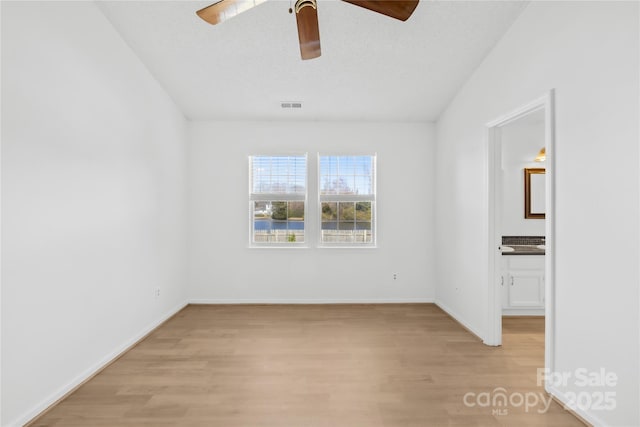 spare room featuring baseboards, light wood-style flooring, visible vents, and a ceiling fan