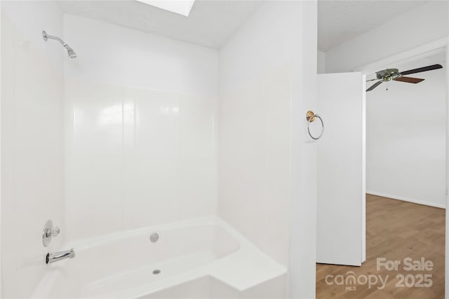 full bathroom with a skylight, a ceiling fan, wood finished floors, and bathing tub / shower combination