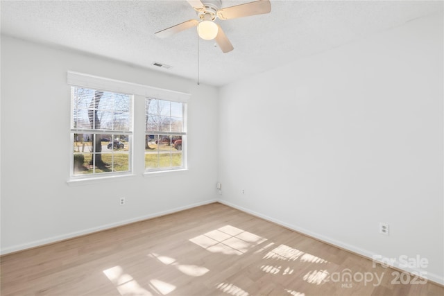 unfurnished room featuring a textured ceiling, a ceiling fan, visible vents, baseboards, and light wood finished floors