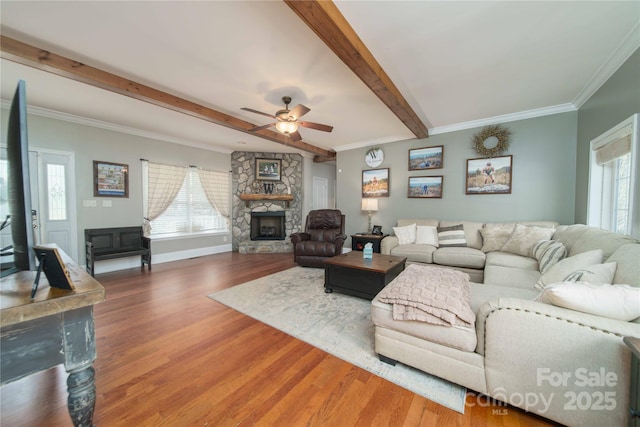 living area with beam ceiling, a healthy amount of sunlight, a stone fireplace, and wood finished floors