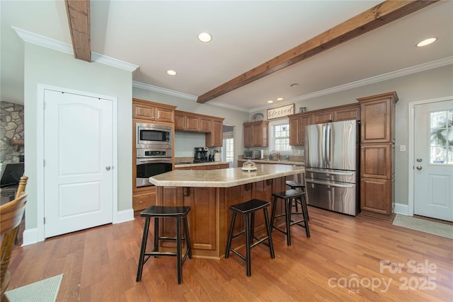 kitchen with a breakfast bar area, light wood-style flooring, appliances with stainless steel finishes, a center island, and beamed ceiling