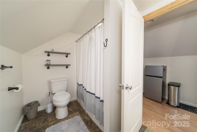 bathroom with toilet, stone finish floor, baseboards, and lofted ceiling