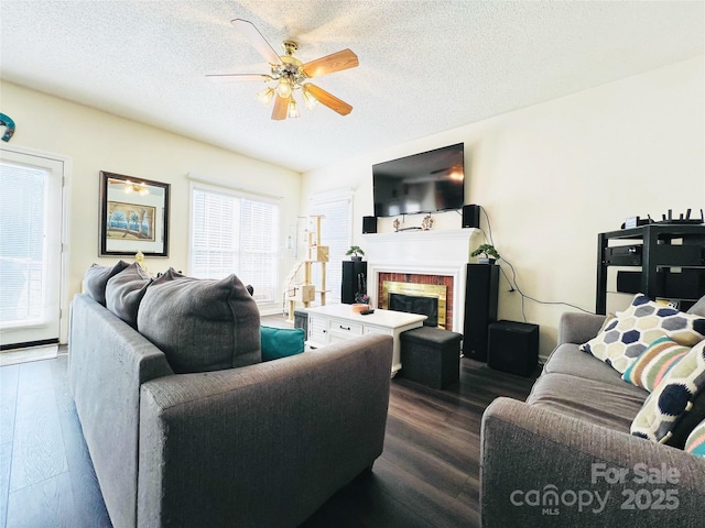 living area featuring dark wood-style floors, a brick fireplace, a ceiling fan, and a textured ceiling