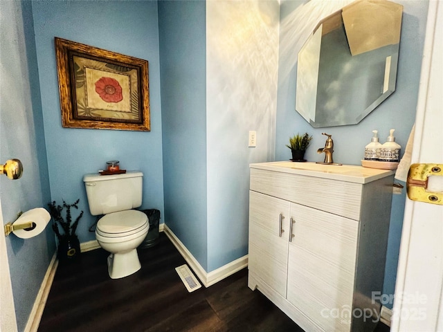 bathroom featuring visible vents, baseboards, toilet, wood finished floors, and vanity