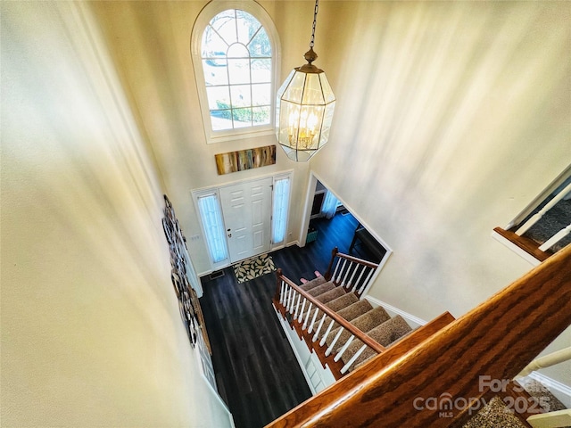 foyer featuring a towering ceiling, dark wood-style floors, stairs, and a notable chandelier