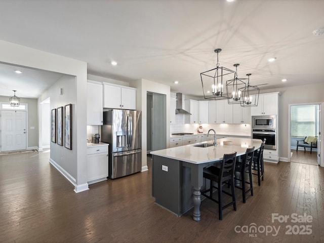 kitchen featuring dark wood-type flooring, a sink, tasteful backsplash, stainless steel appliances, and wall chimney exhaust hood