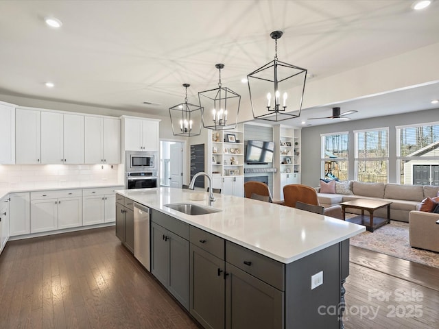 kitchen with a sink, appliances with stainless steel finishes, a center island with sink, and dark wood finished floors