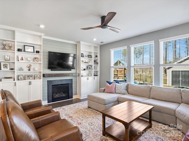 living area with ceiling fan, wood finished floors, a healthy amount of sunlight, and a large fireplace