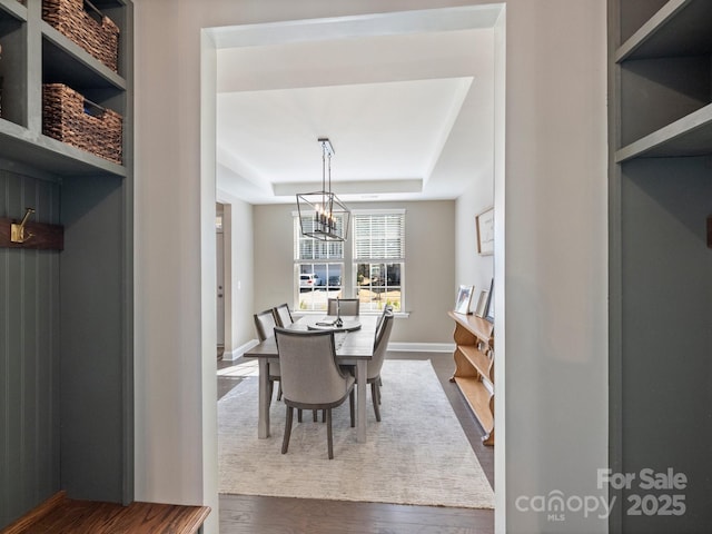 dining room with baseboards, a raised ceiling, an inviting chandelier, and wood finished floors