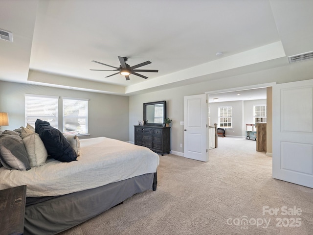 bedroom featuring a tray ceiling, visible vents, baseboards, and light carpet