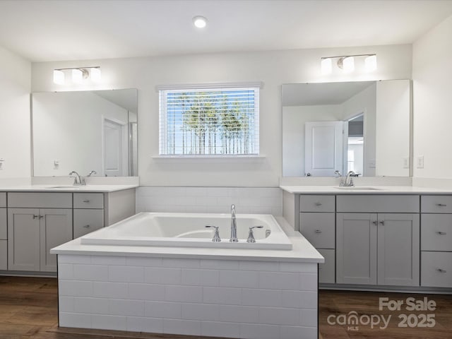 bathroom featuring a sink, wood finished floors, two vanities, and a bath