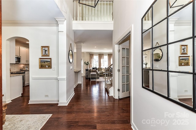 foyer with crown molding, dark wood-type flooring, baseboards, a high ceiling, and ornate columns