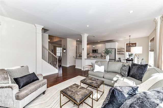 living area featuring stairway, plenty of natural light, dark wood-style floors, and ornate columns