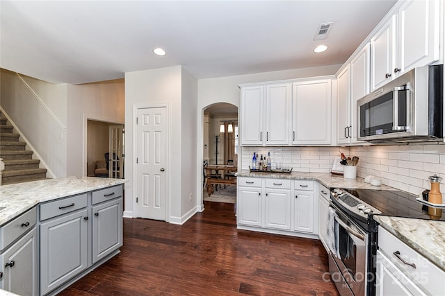 kitchen featuring gray cabinetry, tasteful backsplash, dark wood finished floors, arched walkways, and appliances with stainless steel finishes