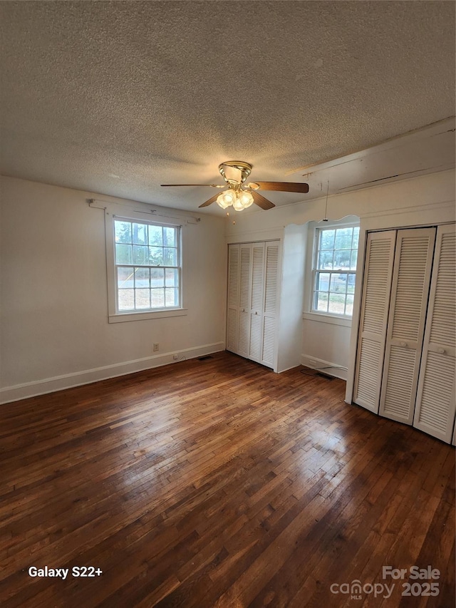 unfurnished bedroom featuring dark wood-style floors, two closets, ceiling fan, a textured ceiling, and baseboards