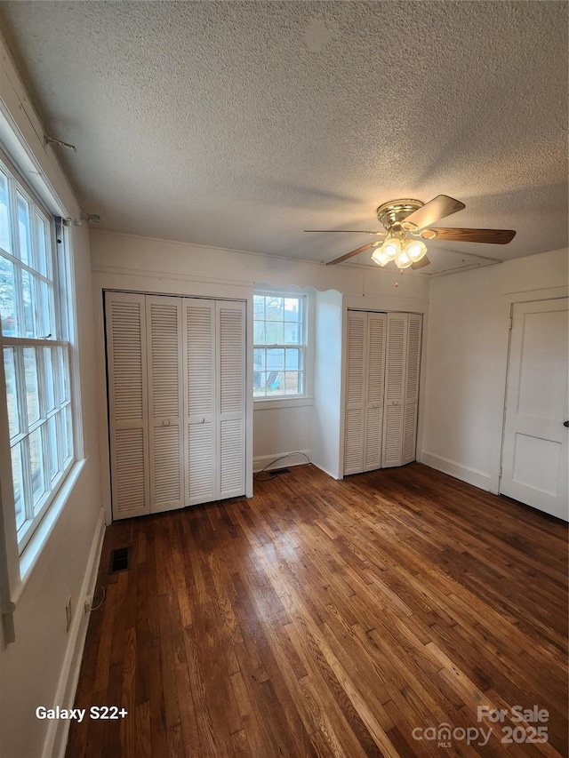 unfurnished bedroom with wood-type flooring, a textured ceiling, baseboards, and two closets