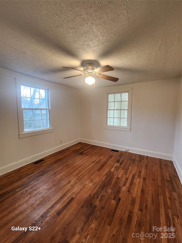 spare room with dark wood-style floors, baseboards, visible vents, and ceiling fan