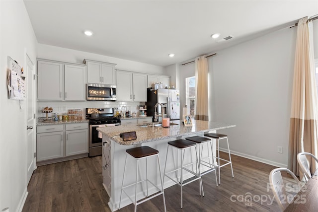 kitchen featuring a kitchen bar, a center island with sink, a sink, tasteful backsplash, and appliances with stainless steel finishes