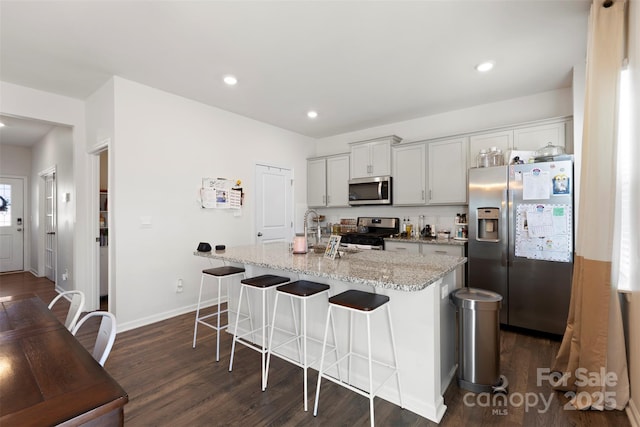 kitchen featuring dark wood-type flooring, an island with sink, a kitchen breakfast bar, stainless steel appliances, and a sink