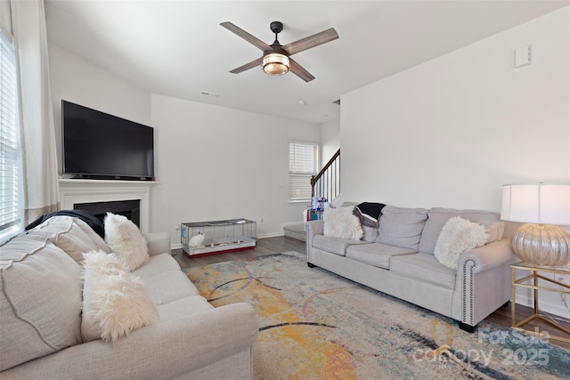 living room featuring stairway, baseboards, wood finished floors, and a ceiling fan