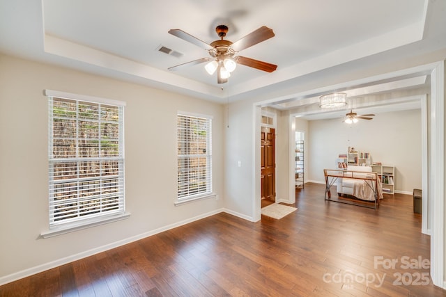 bedroom with a tray ceiling, baseboards, visible vents, and wood-type flooring