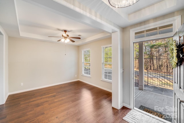 entrance foyer featuring ceiling fan with notable chandelier, a tray ceiling, baseboards, and dark wood-type flooring