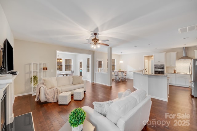 living room featuring visible vents, baseboards, dark wood-style floors, and a ceiling fan