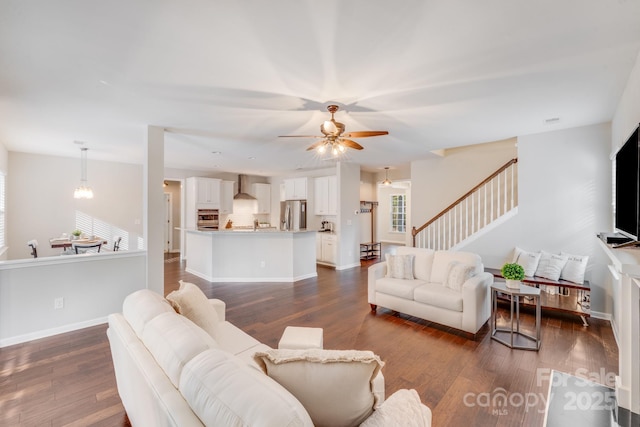 living area featuring a ceiling fan, baseboards, dark wood-type flooring, and stairs