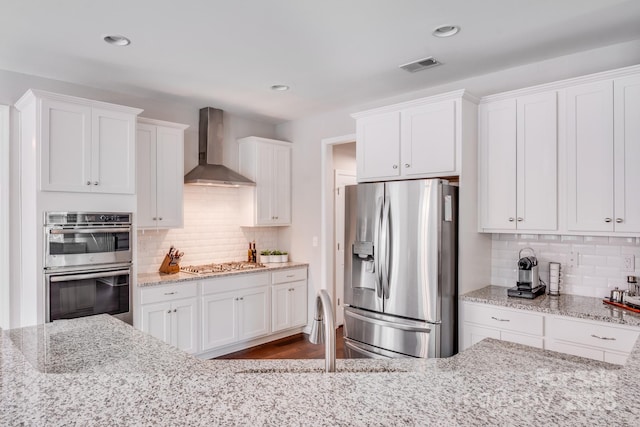 kitchen with light stone countertops, a sink, stainless steel appliances, white cabinets, and wall chimney exhaust hood