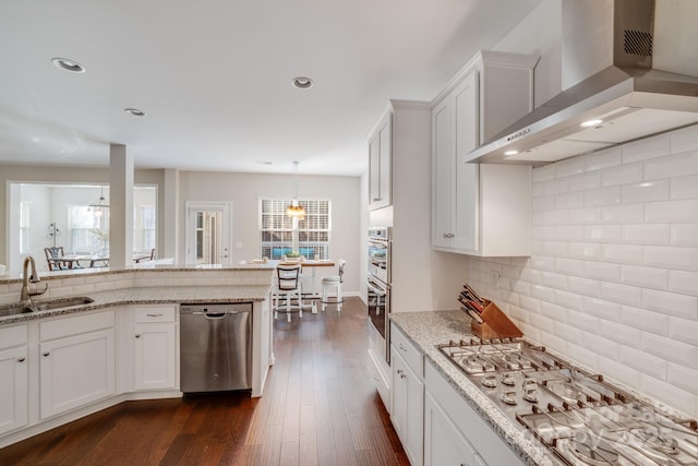 kitchen with a sink, appliances with stainless steel finishes, wall chimney range hood, decorative backsplash, and dark wood-style flooring