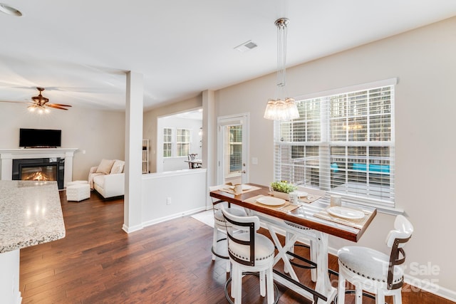 dining space featuring dark wood-style floors, baseboards, visible vents, ceiling fan, and a glass covered fireplace