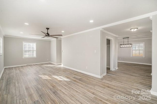 spare room with light wood-type flooring, a healthy amount of sunlight, baseboards, and crown molding