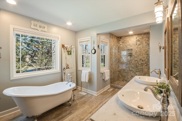 bathroom featuring wood finished floors, a freestanding bath, tiled shower, and a sink