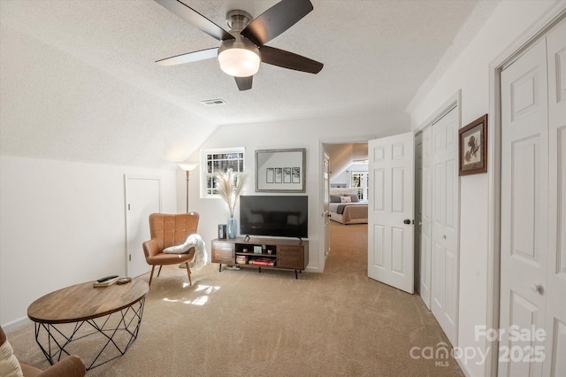 living area with visible vents, ceiling fan, vaulted ceiling, a textured ceiling, and carpet flooring