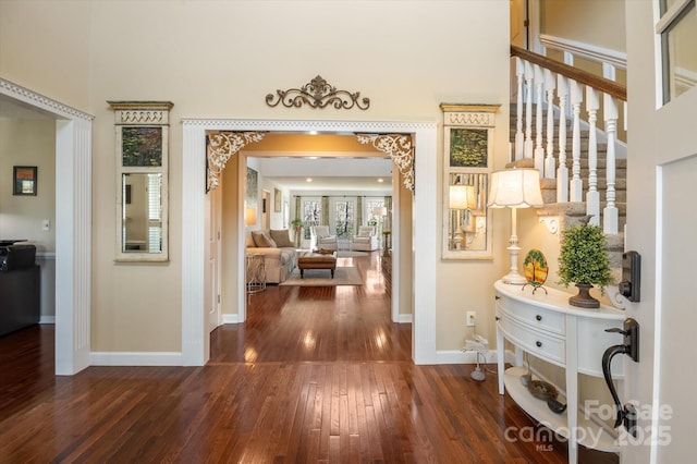 entrance foyer with arched walkways, baseboards, a towering ceiling, and hardwood / wood-style floors