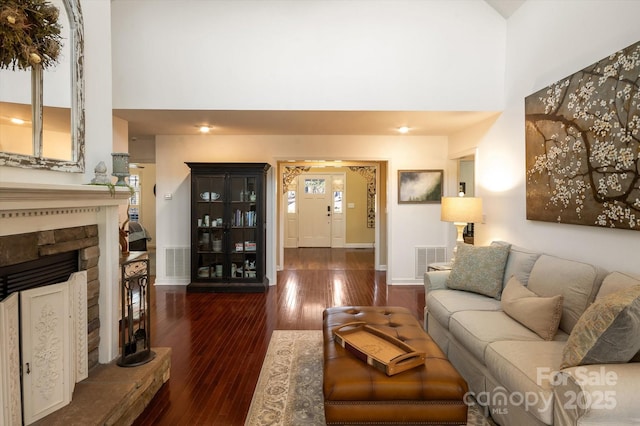 living room with visible vents, a fireplace with raised hearth, hardwood / wood-style floors, and a towering ceiling